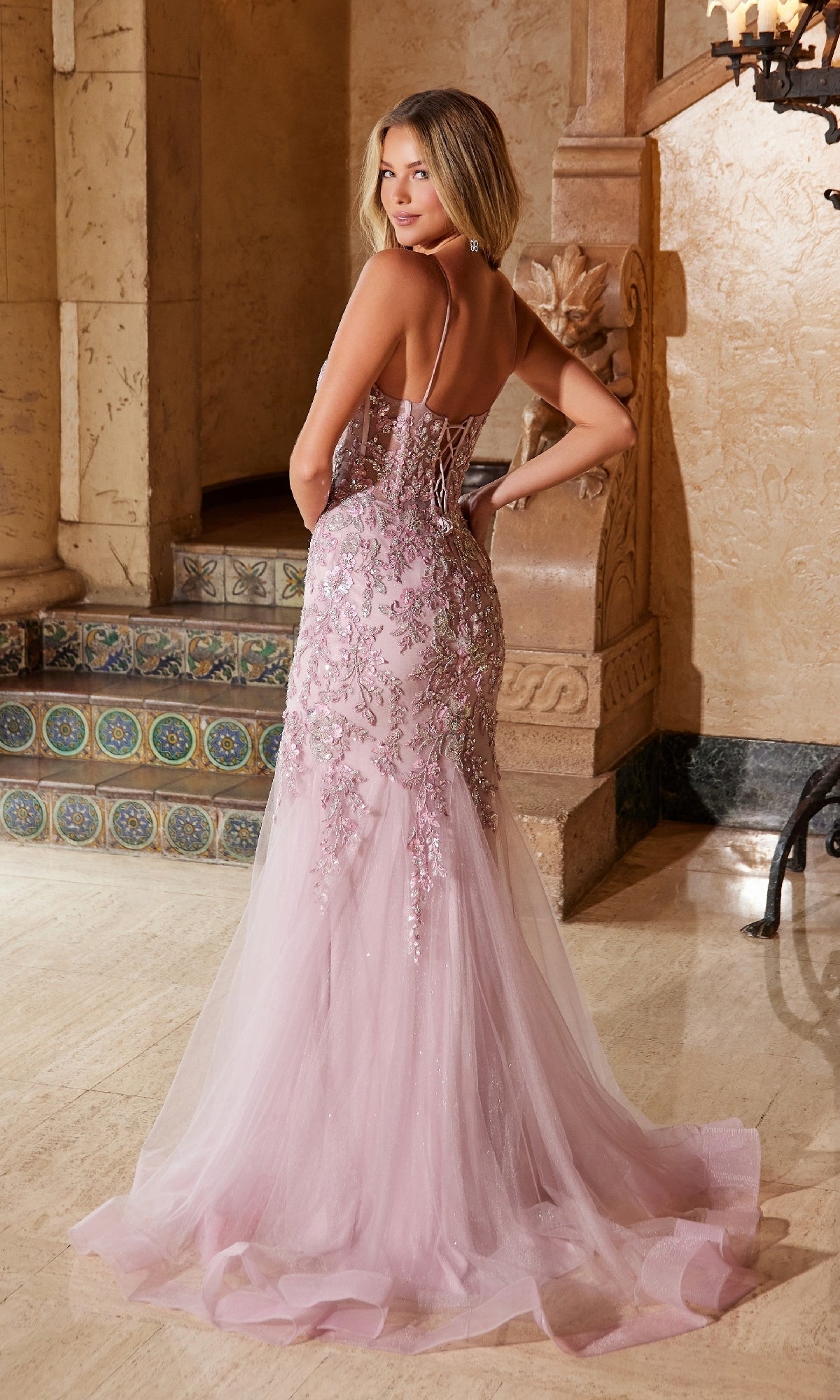 A woman models the Nox Anabel Q1541—an elegant, floor-length light pink prom dress with floral embroidery, a lace-up back, and a shimmering train. This stunning gown is perfect for prom.